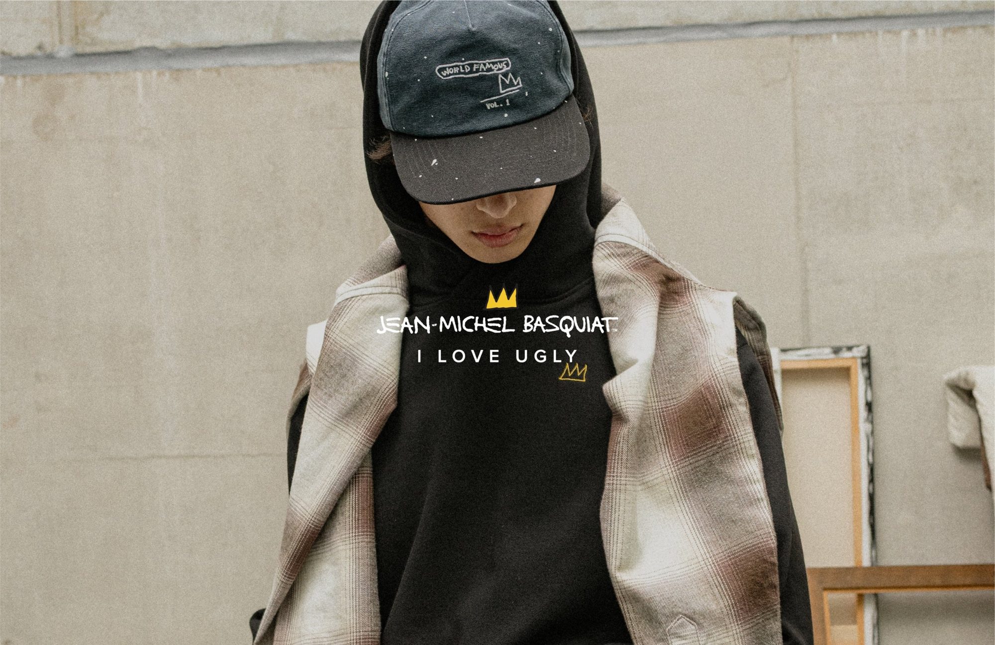 Model in a black hoodie, painted cap and ombré flannel, with the Jean-Michel Basquiat and I Love Ugly logos