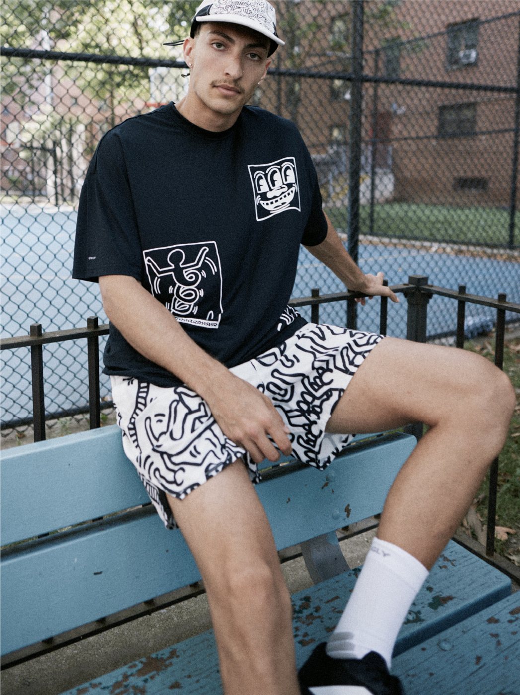 I Love Ugly x Keith Haring: Black graphic tee and Keith Haring print shorts on a bench