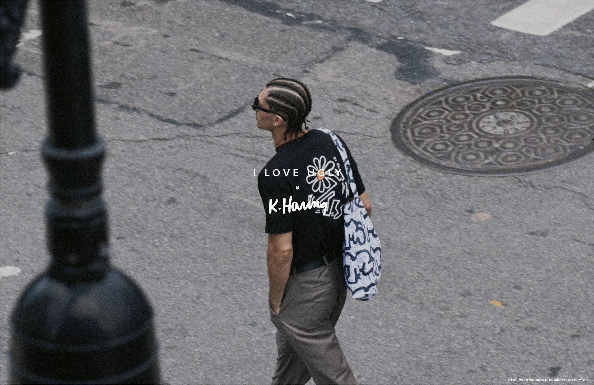 Model crossing a New York street in a K. Haring print tee with a printed tote, under the I Love Ugly x K. Haring logo