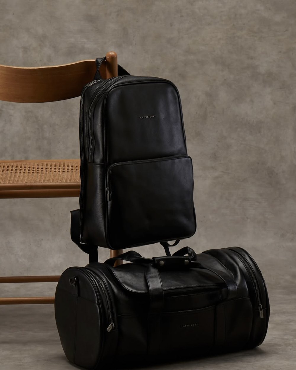 Black leather backpack hung on a wooden chair above the matching leather duffle