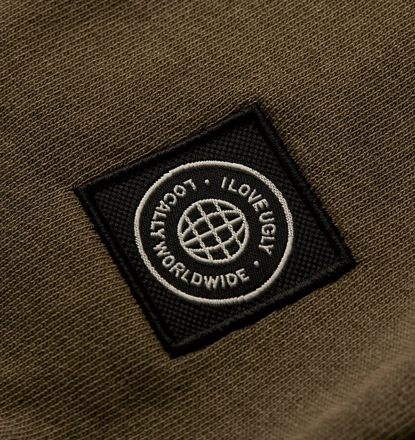 Close-up of the woven globe badge on the washed olive fleece
