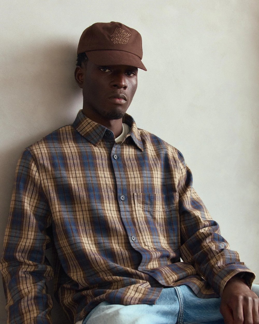Blue and brown plaid flannel shirt worn with a brown cap and light wash denim