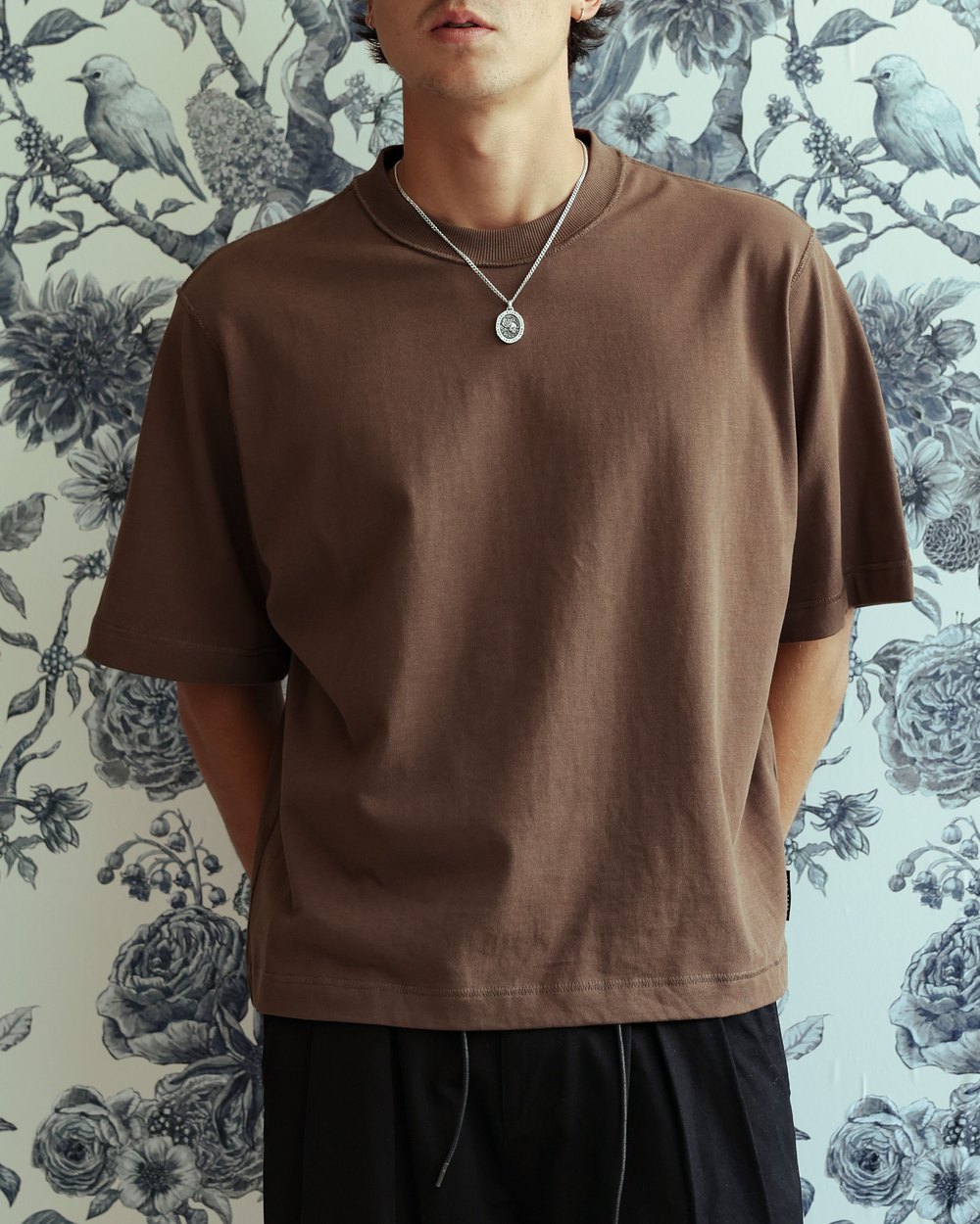 Brown crop box tee worn against a floral wallpaper