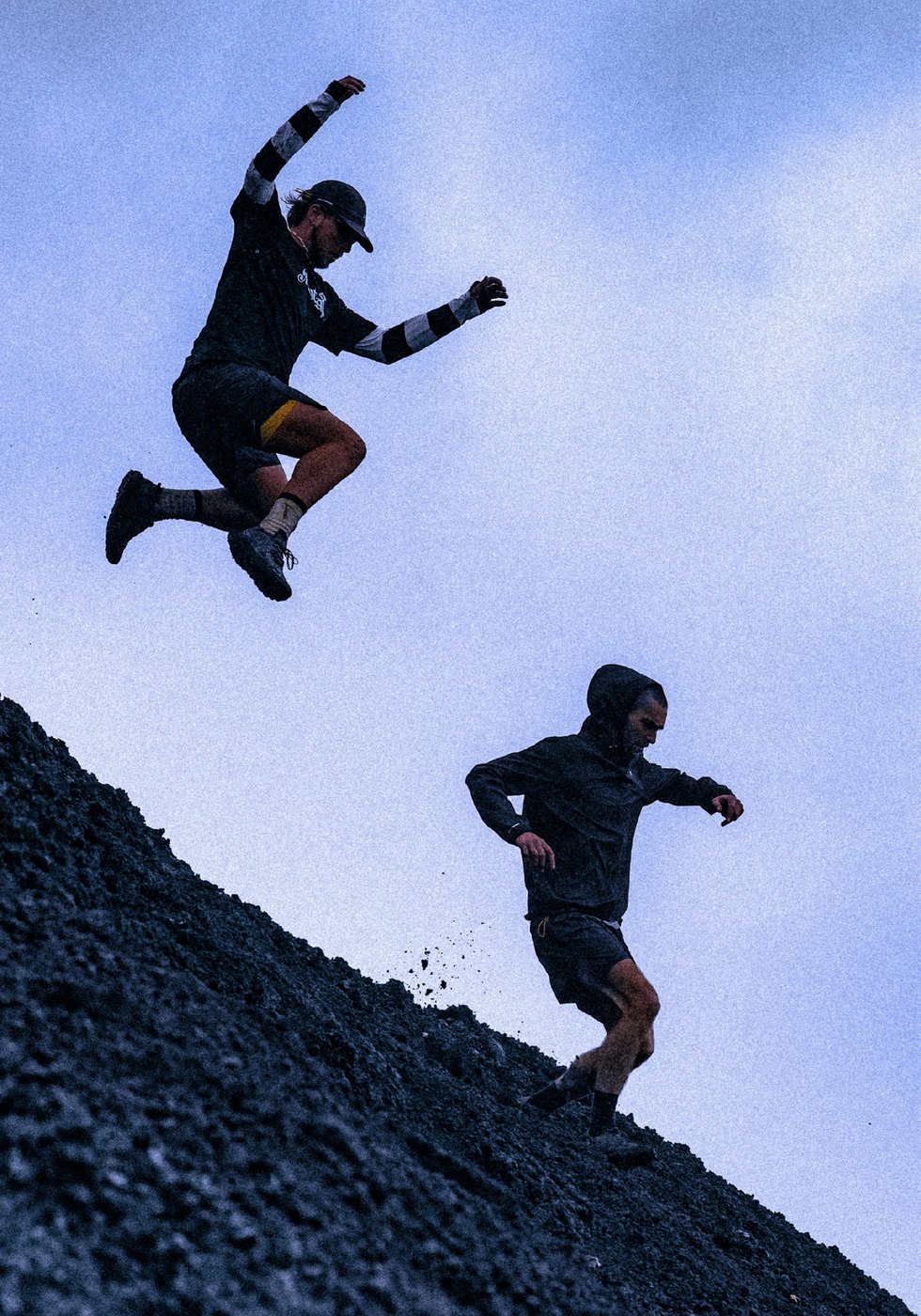 Two runners leaping down a black scree slope in the collection