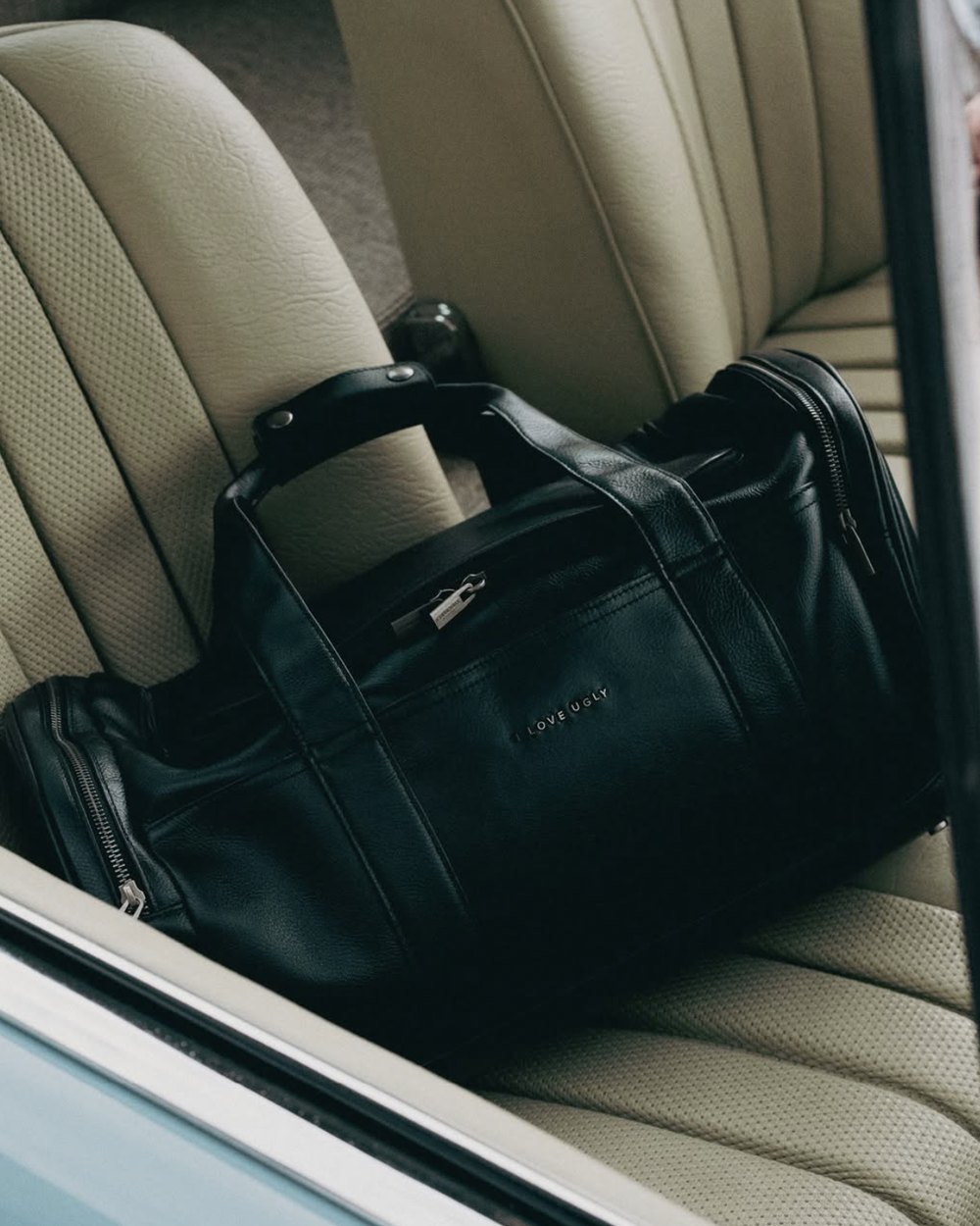 Black leather duffle bag on a cream vintage car seat