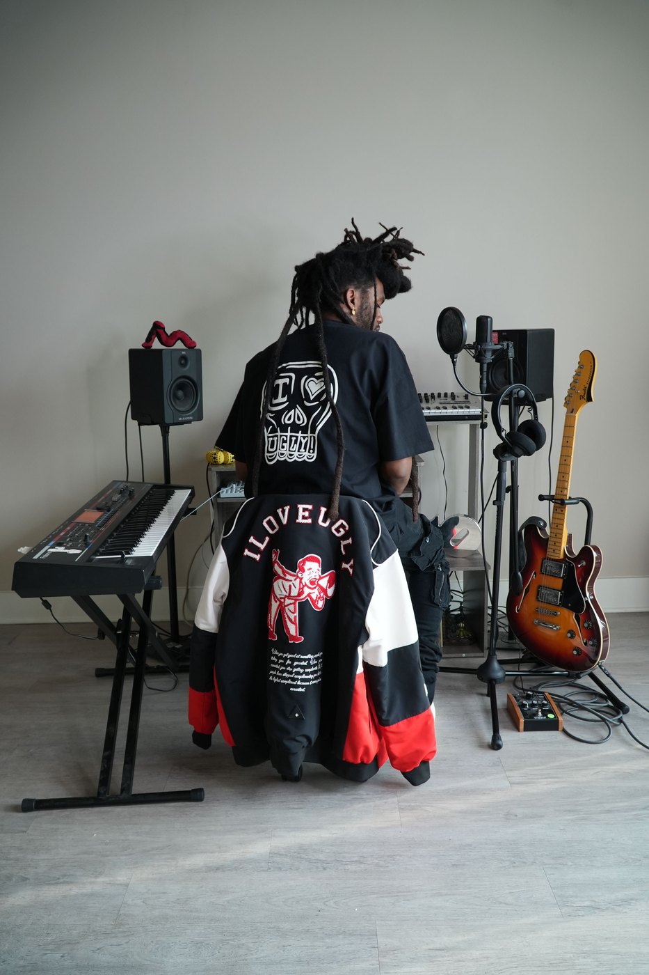 Musician in a home studio wearing the I Love Ugly skull tee, with the racing jacket over the chair