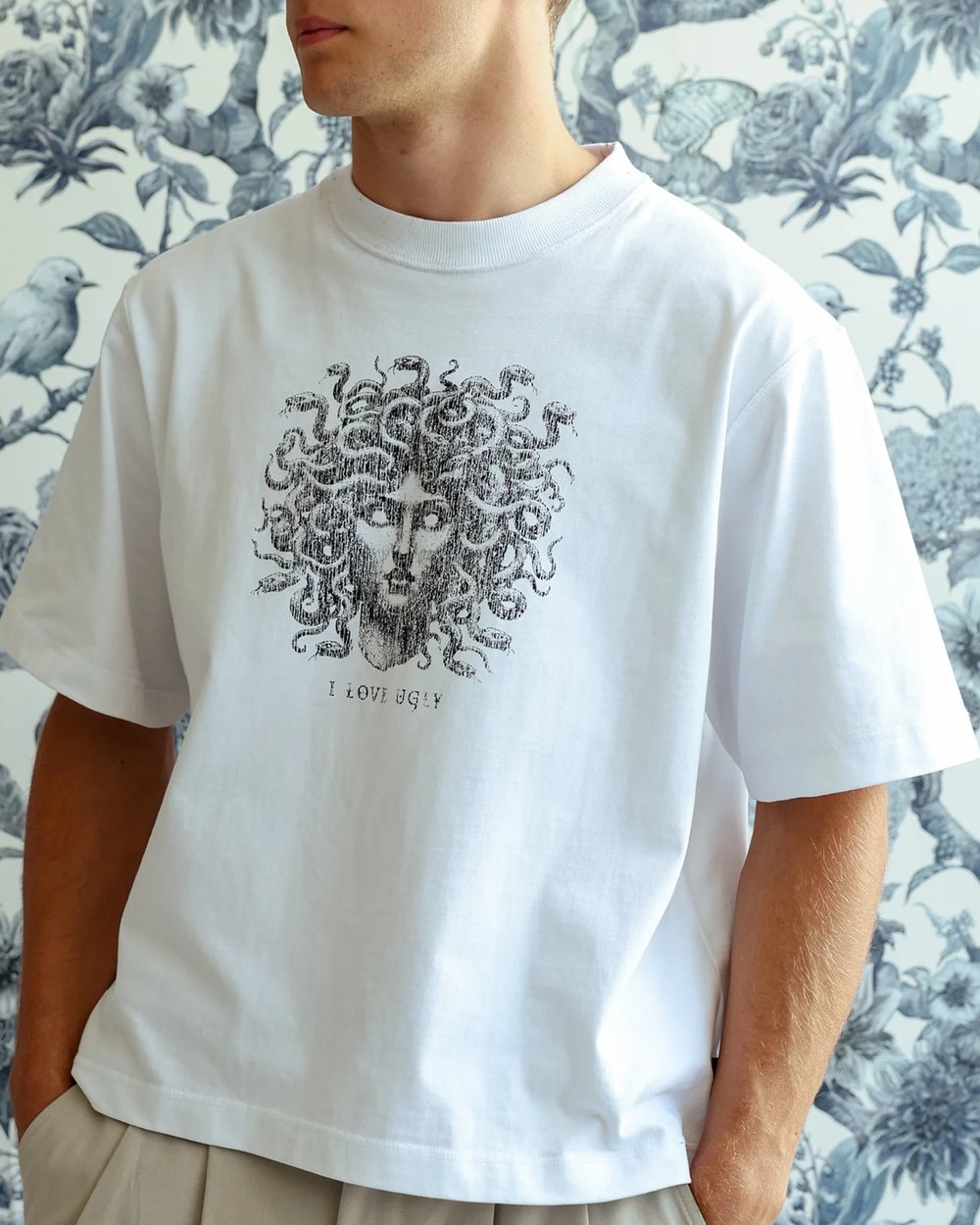 White Medusa graphic tee worn against a floral wallpaper