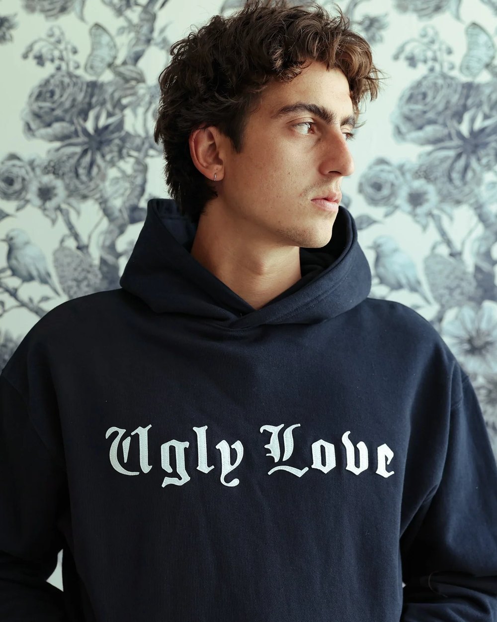 Navy Ugly Love hood worn against a floral wallpaper