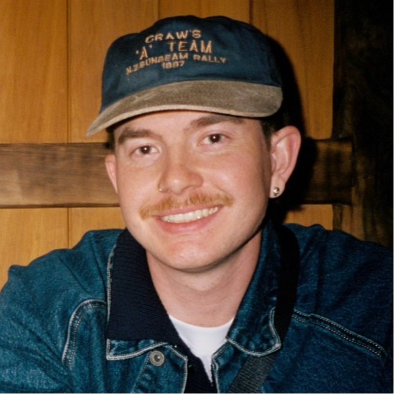 Portrait of Judd Cargin smiling, wearing a navy cap and denim jacket