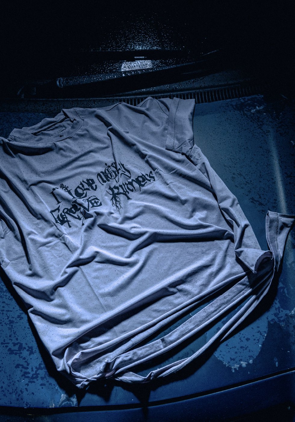 Grey mesh Grave Runners tee laid on a wet car bonnet