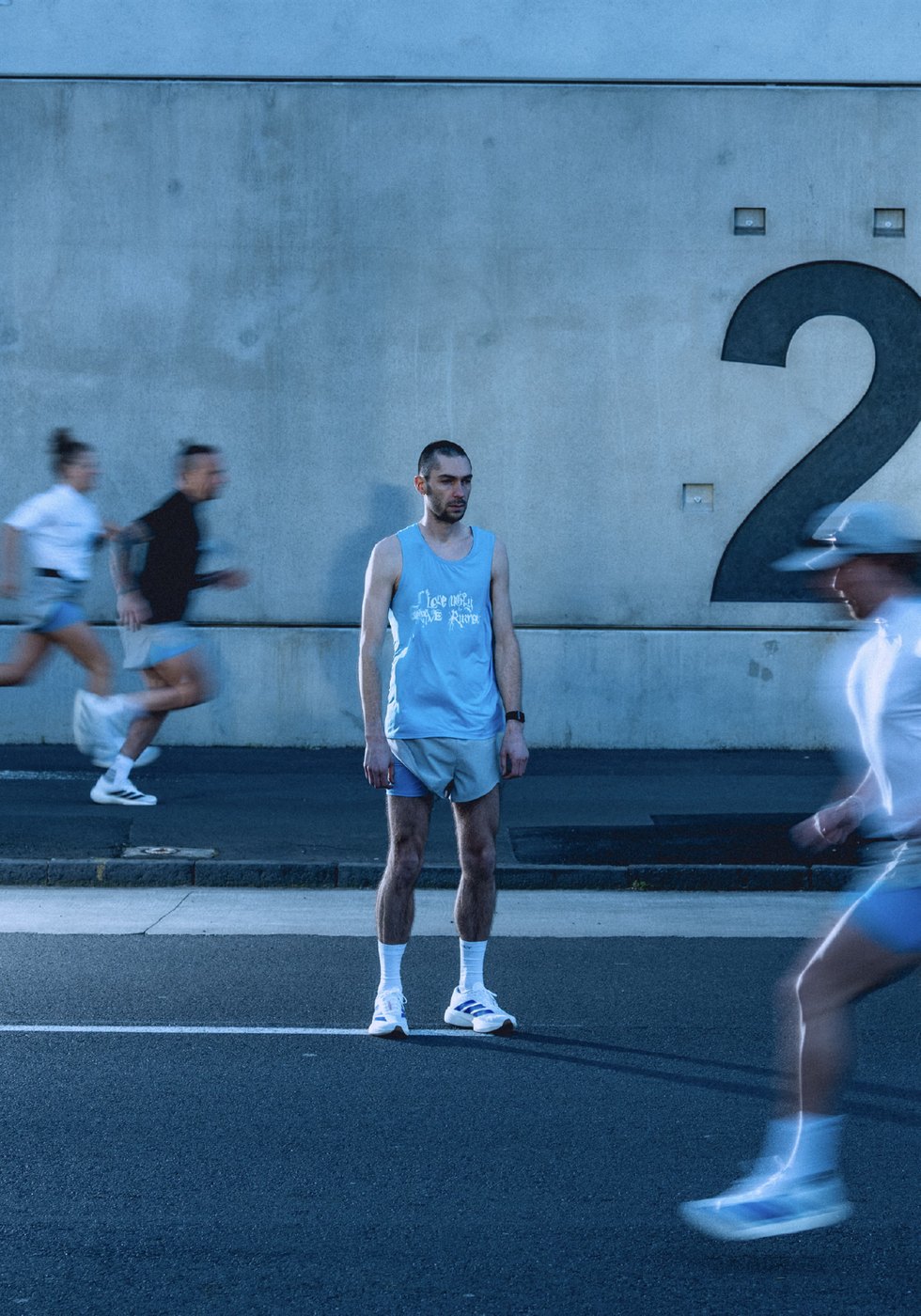Runner in the blue Grave Runners singlet and split shorts standing as others run past