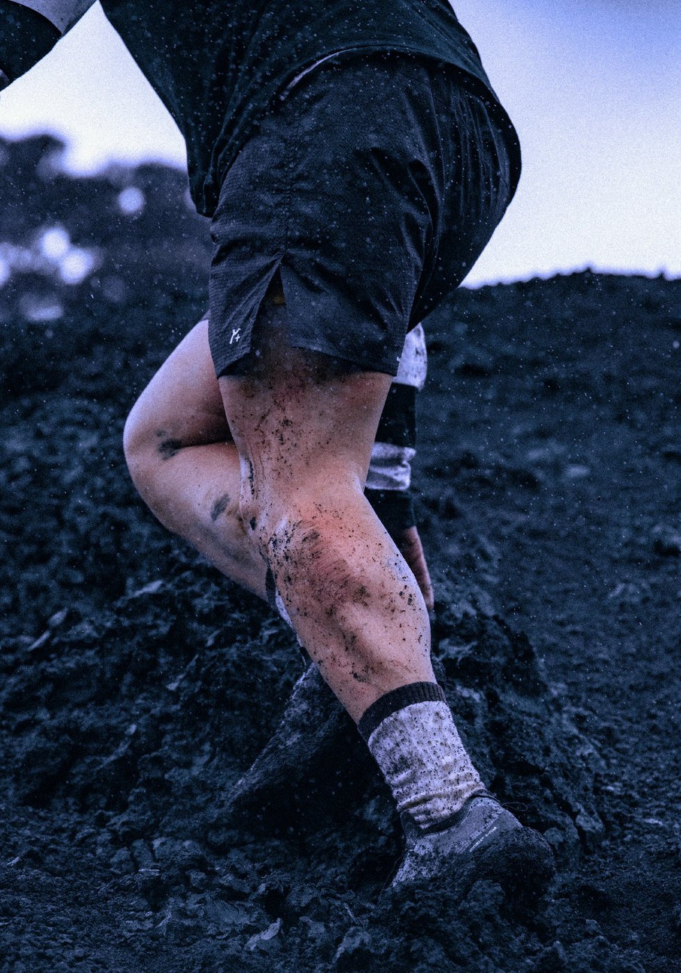 Close up of mud splattered legs in black split shorts climbing a dirt slope