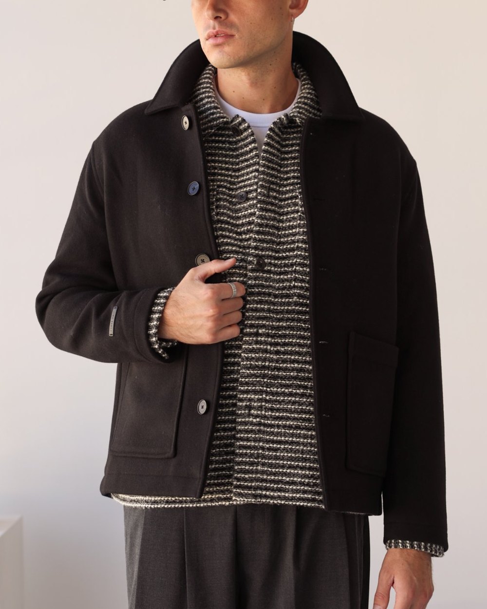Black melton wool chore jacket worn open over a striped knit overshirt