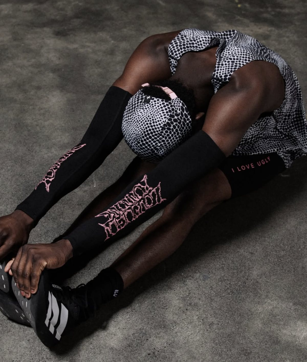 Athlete stretching in a dot-print cap, singlet and shorts with printed arm and leg sleeves