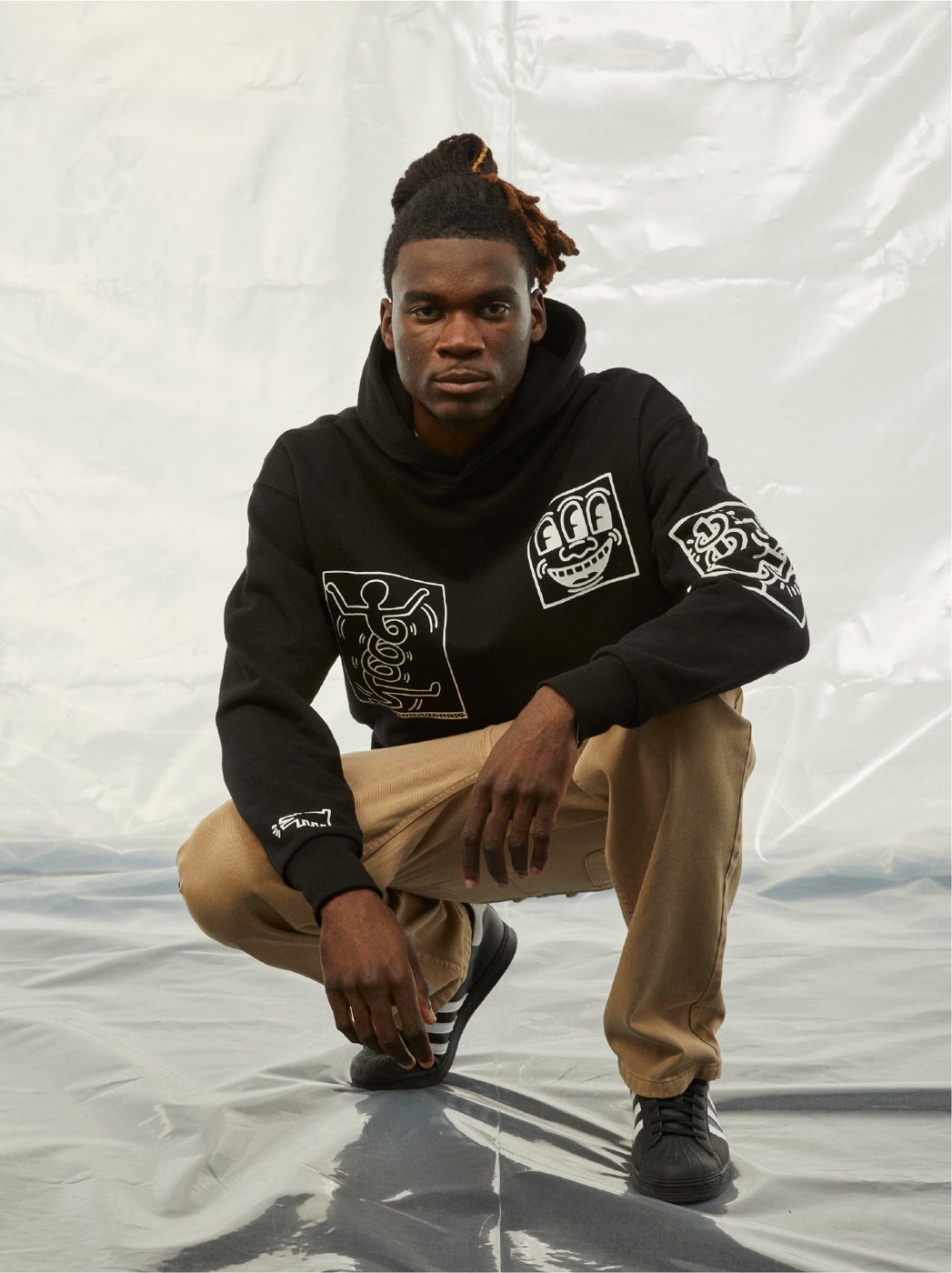 I Love Ugly x Keith Haring: Black Keith Haring hoodie with tan pants, crouching