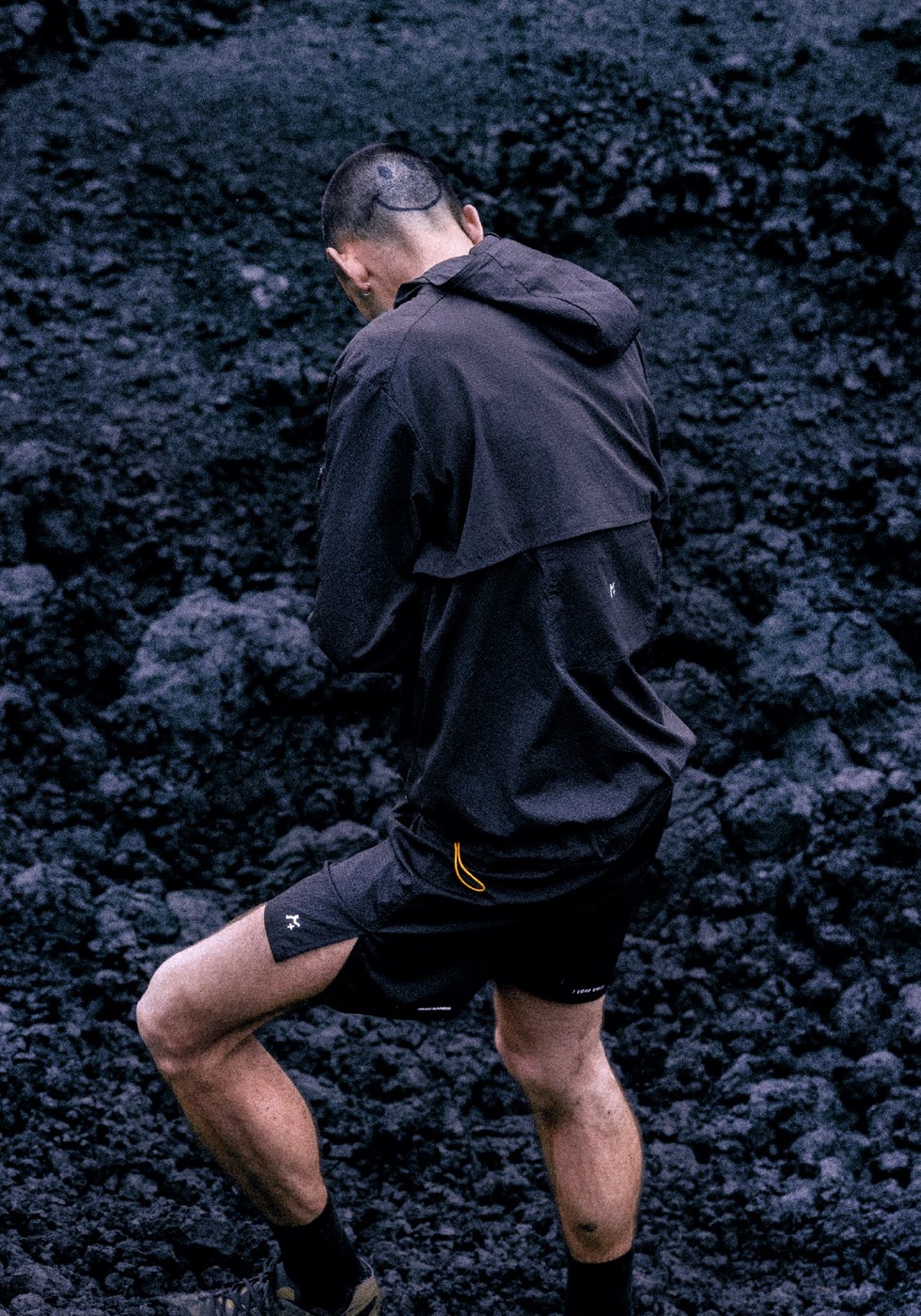 Black hooded running jacket and split shorts against volcanic rock