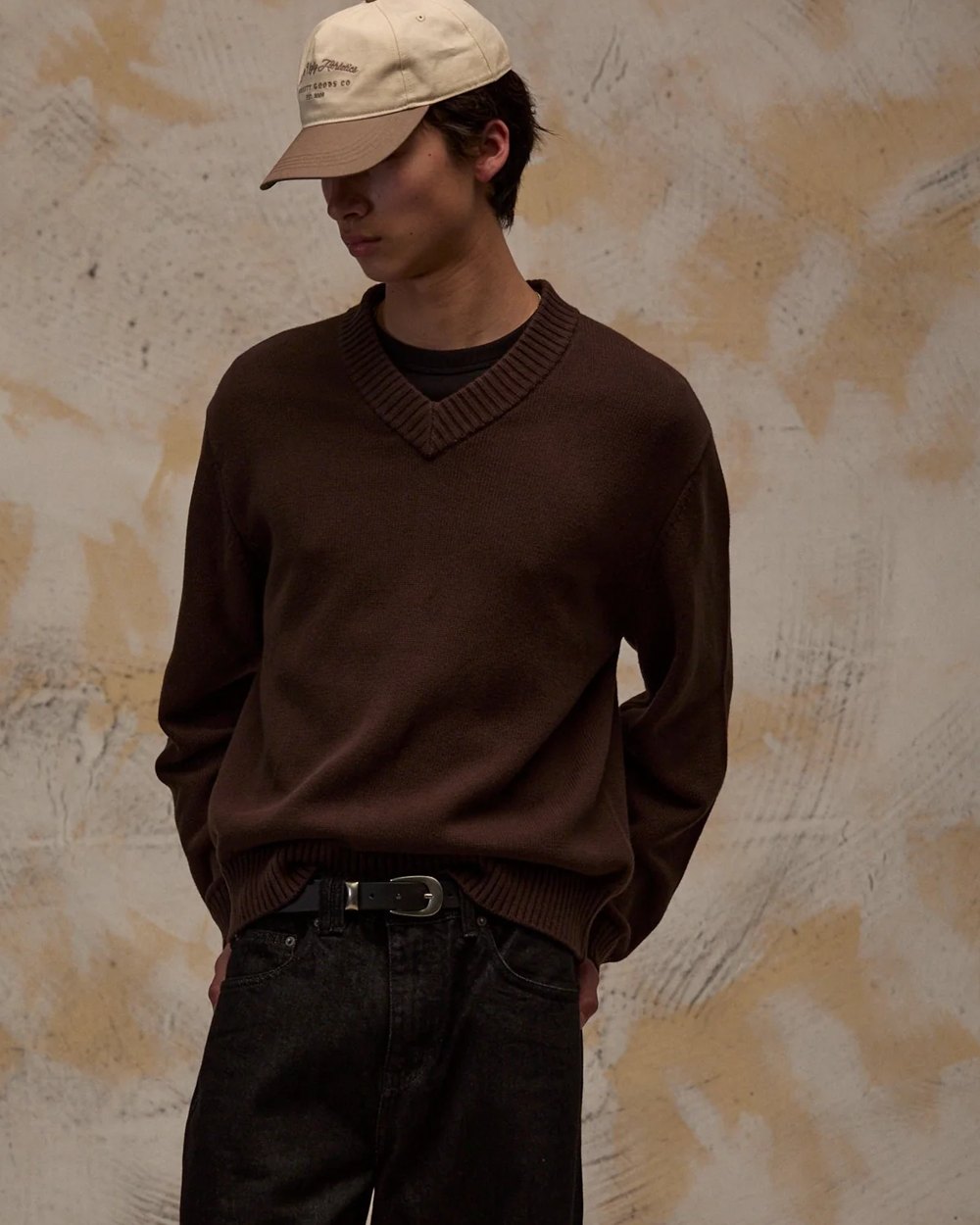 Chocolate brown V neck sweater worn with black denim and a cream cap